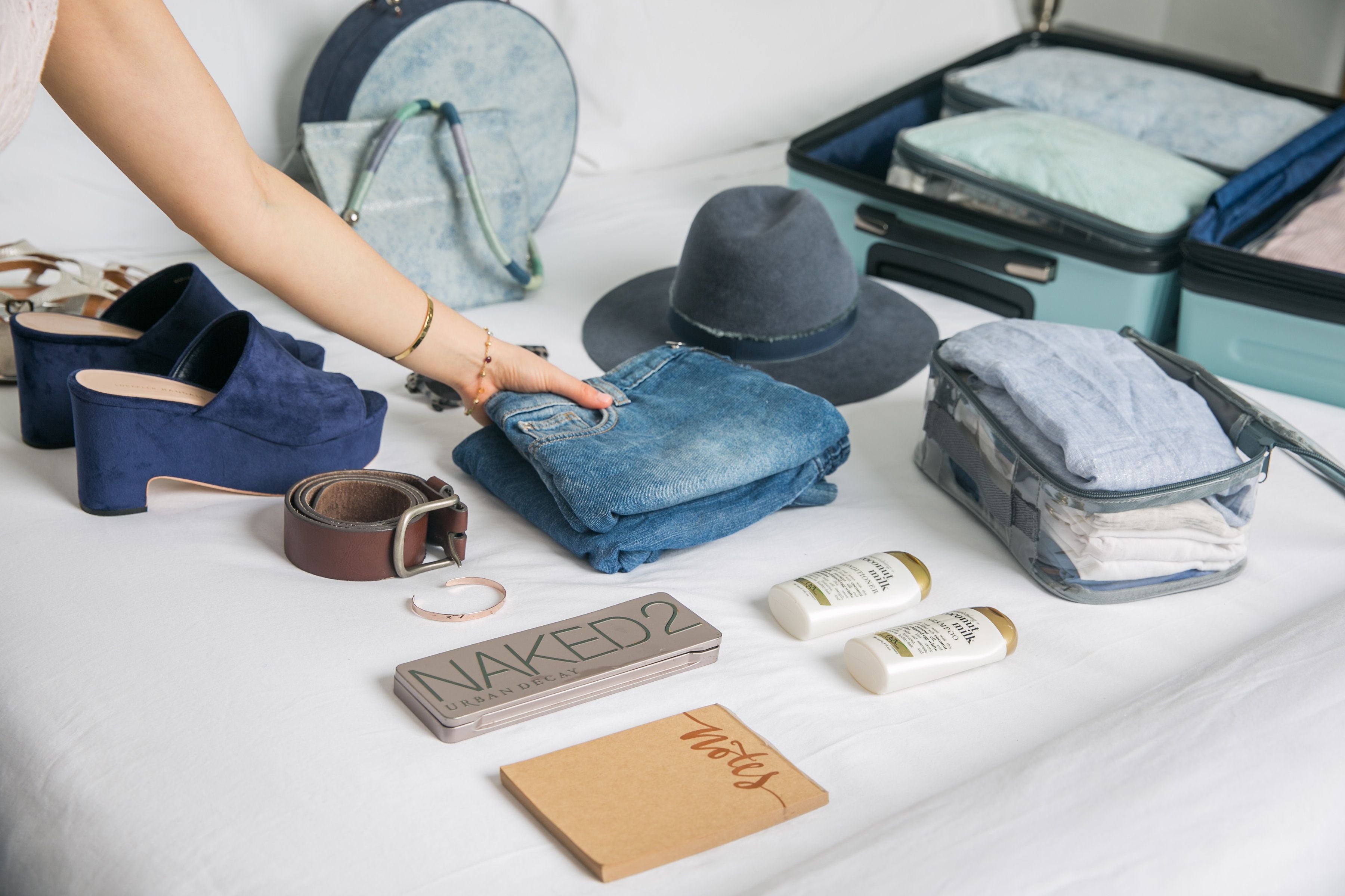 Travel essentials and jeans laid out on the bed with clear packing cubes