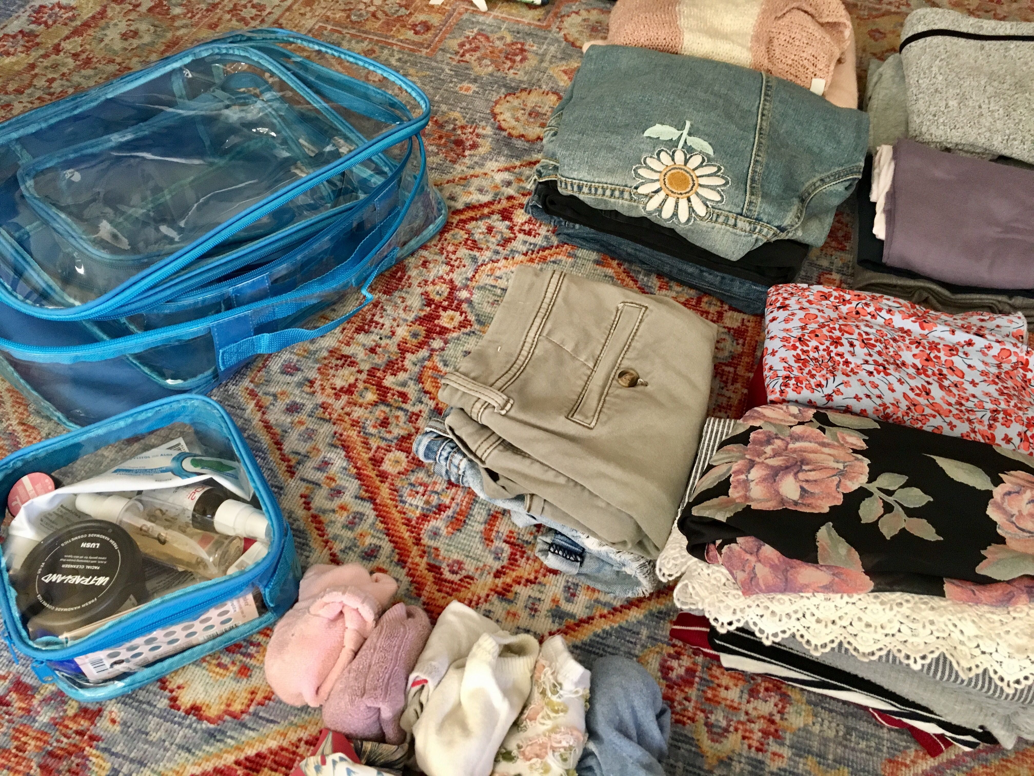 Folded clothes and turquoise clear packing cubes on the floor