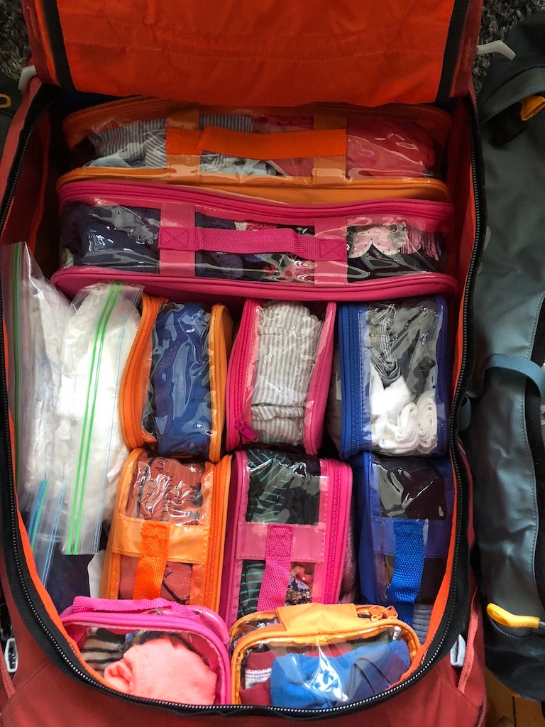 Pink and orange color coded packing cubes for kids inside suitcase