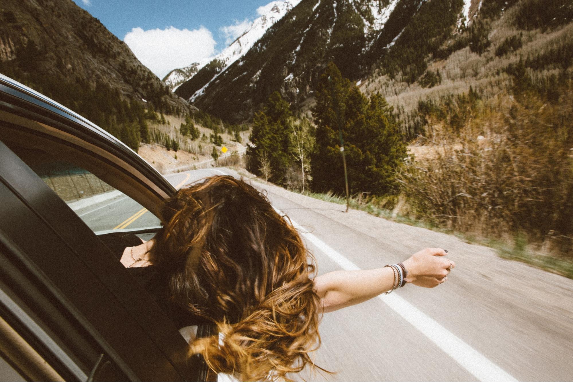 Young girl with her head and right hand out of the car on a road trip