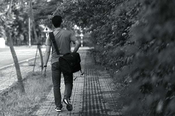 man walking path with messenger bag black and white