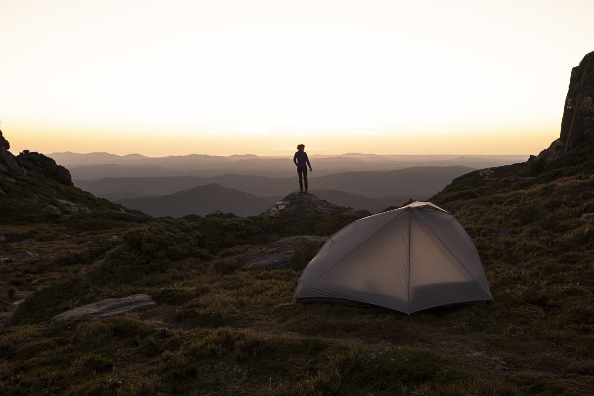 Alto tent in foreground with woman overlooking mountain range in background