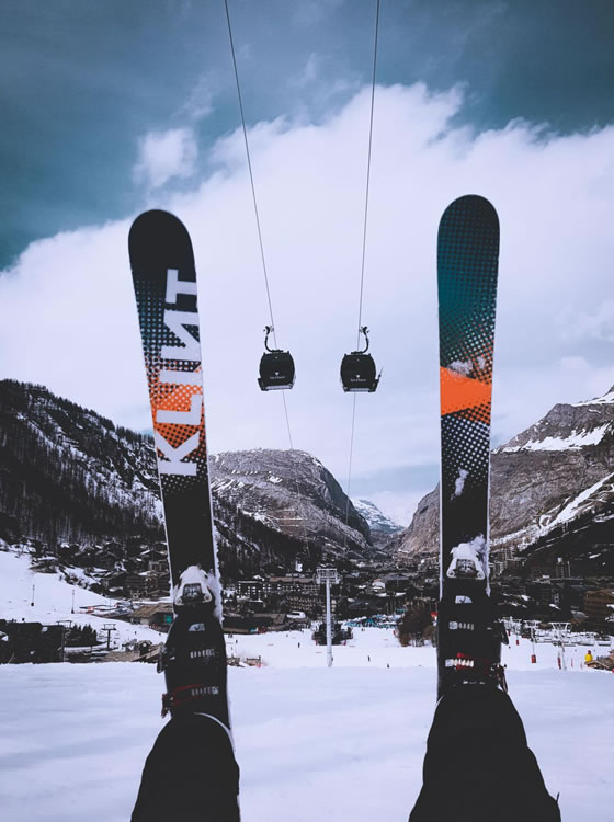 Pair of alpine skis overlooking a snowy resort valley with gondola lifts in the background