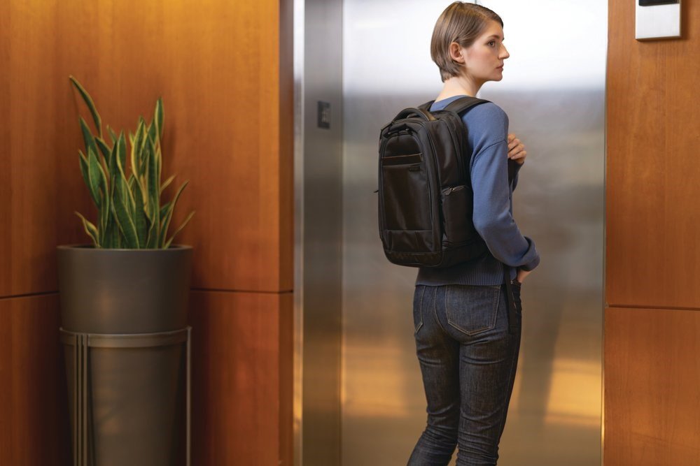 Woman waiting for an elevator and wearing a Junyuan laptop backpack