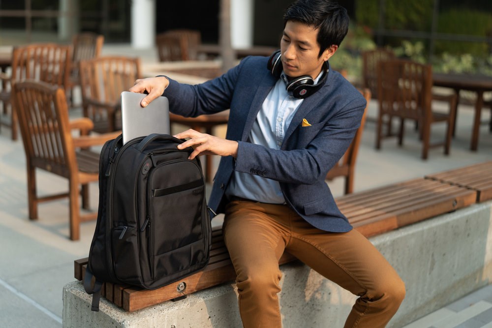 A man putting away a laptop into a Junyuan laptop backpack