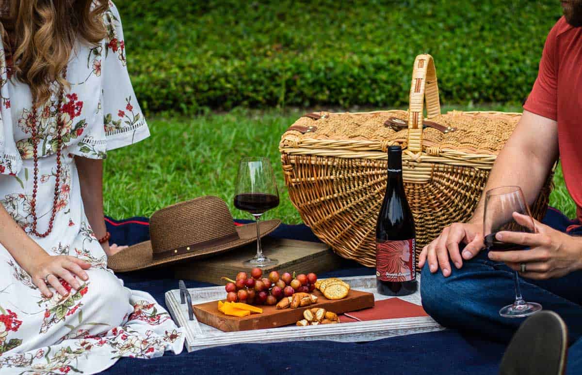 a couple enjoying a picnic on the grass with a classic picnic basket and wine. 