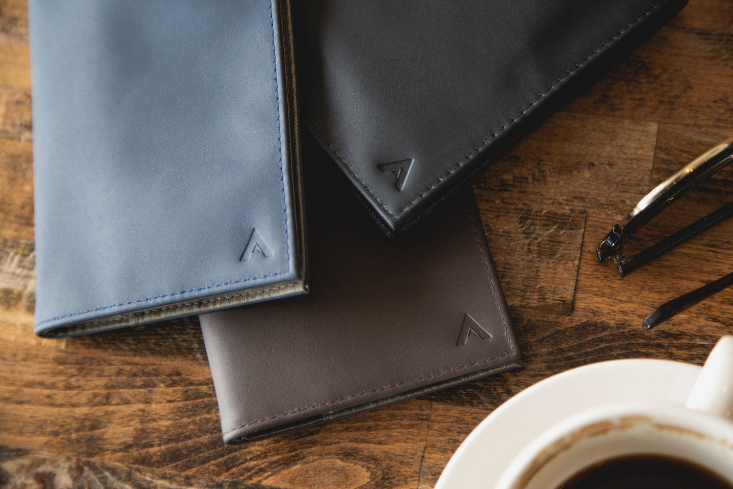 Allett Leather Original Wallets in all colors on a table with coffee - Merlot, Midnight Blue, Onyx Black