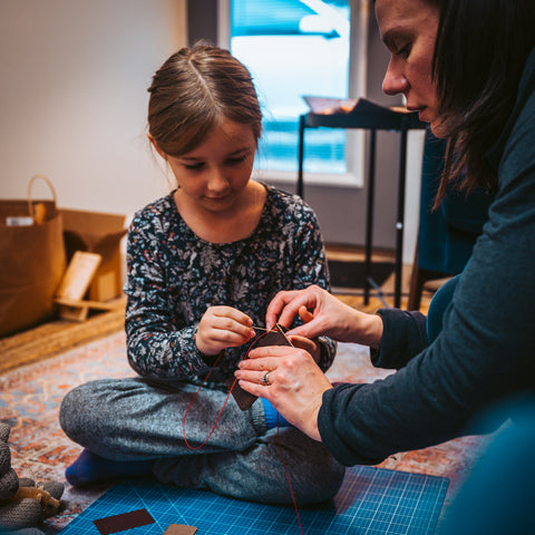 Child learning to sew a leather project with adult supervision