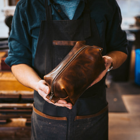 Man in an apron holding a leather toiletry bag