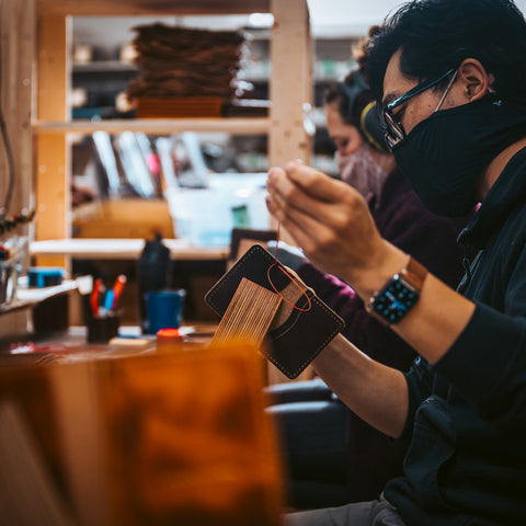 Man wearing a mask while hand-stitching a leather wallet