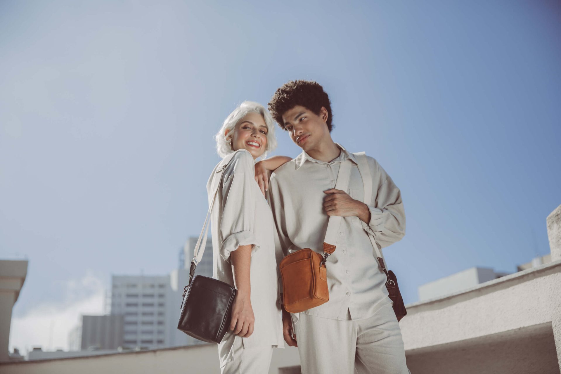 Genderless mini leather messenger pouch in chestnut handcrafted with saddle stitching and full grain vegetable tanned lamb leather with webbed cotton off white crossbody shoulder strap and outer slip pocket carried by millenial man and woman.jpg