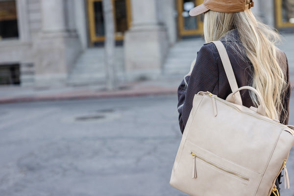 woman with a cream-colored travel diaper backpack on a city street
