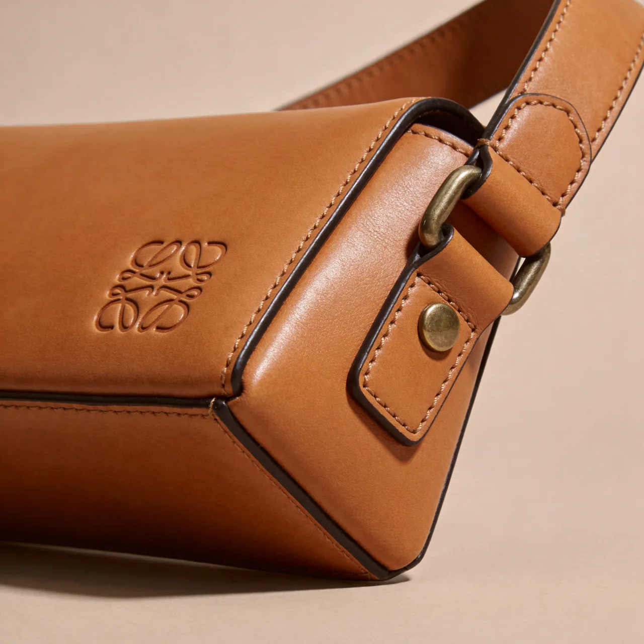 Genuine glove-tanned and pebbled leather handbag with brass hardware and edge finishing, the craft detail behind a Coach or Tory Burch price tag