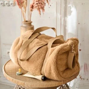 Character plush bag with webbing strap and metal zipper photographed on a rattan table